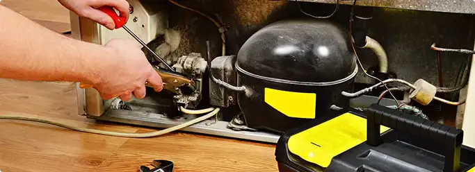 Refrigerator repair technician fixing the compressor and wiring in Clovis, CA