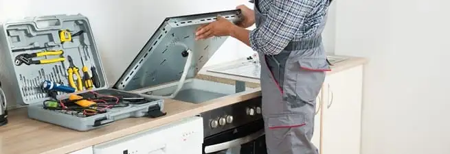 Cooktop repair technician lifting a built-in stovetop for service in Fresno, CA