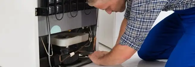 Refrigerator repair technician servicing the compressor and condenser area in Fresno, CA