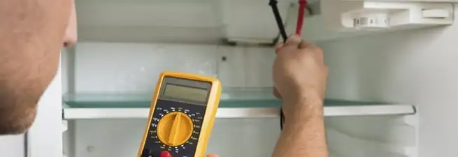 Refrigerator repair technician testing electrical components with a multimeter in Fresno, CA